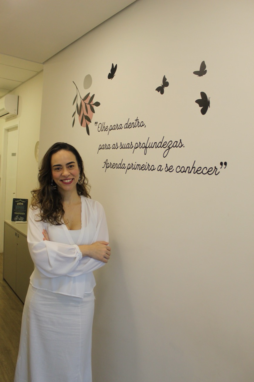 Simone de Siqueira no consultório, ao lado da frase na parede: Olhe para dentro, para as suas profundezas. Aprenda primeiro a se conhecer.